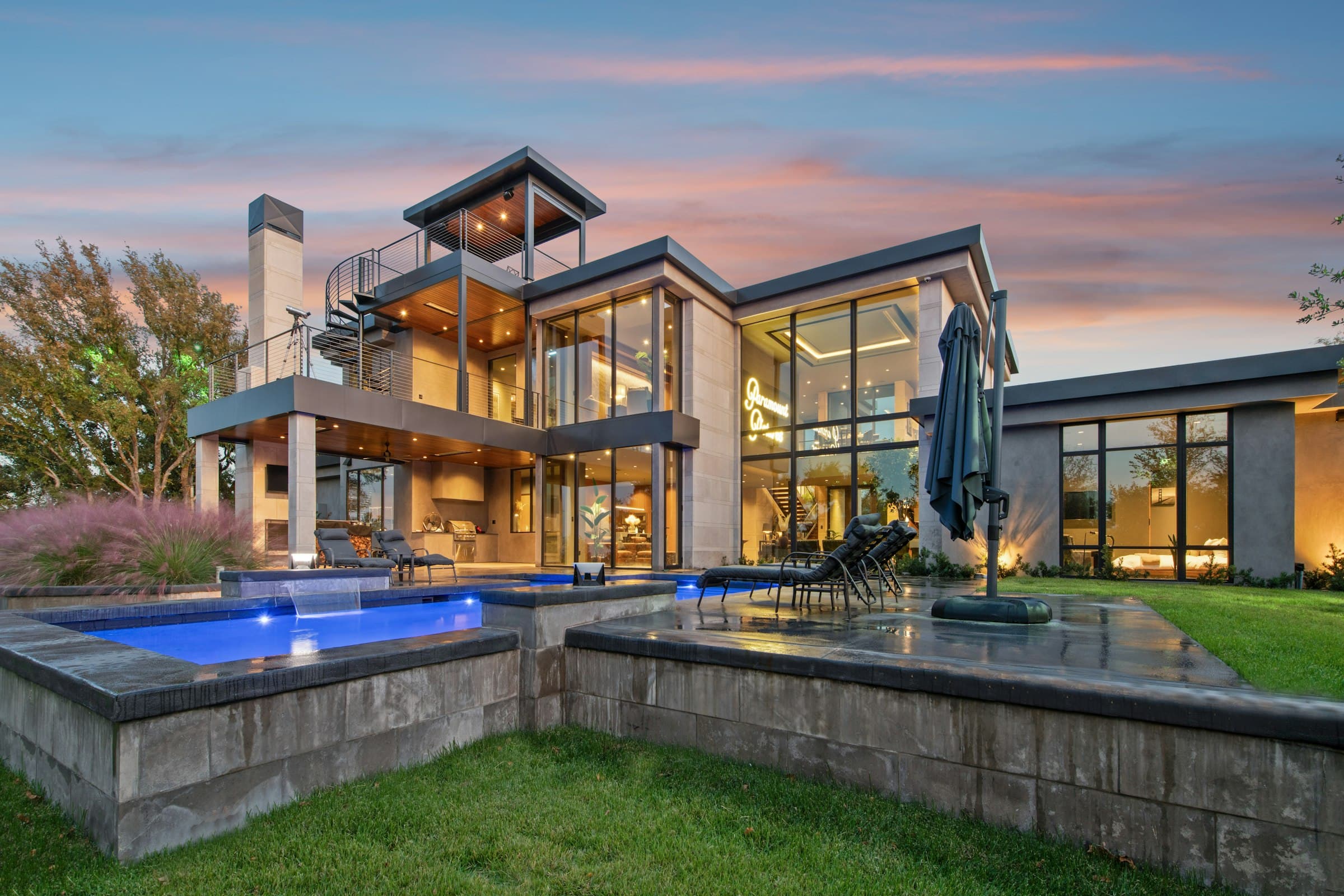 A modern hillside home glowing at dusk, with a terrace and pool overlooking the valley