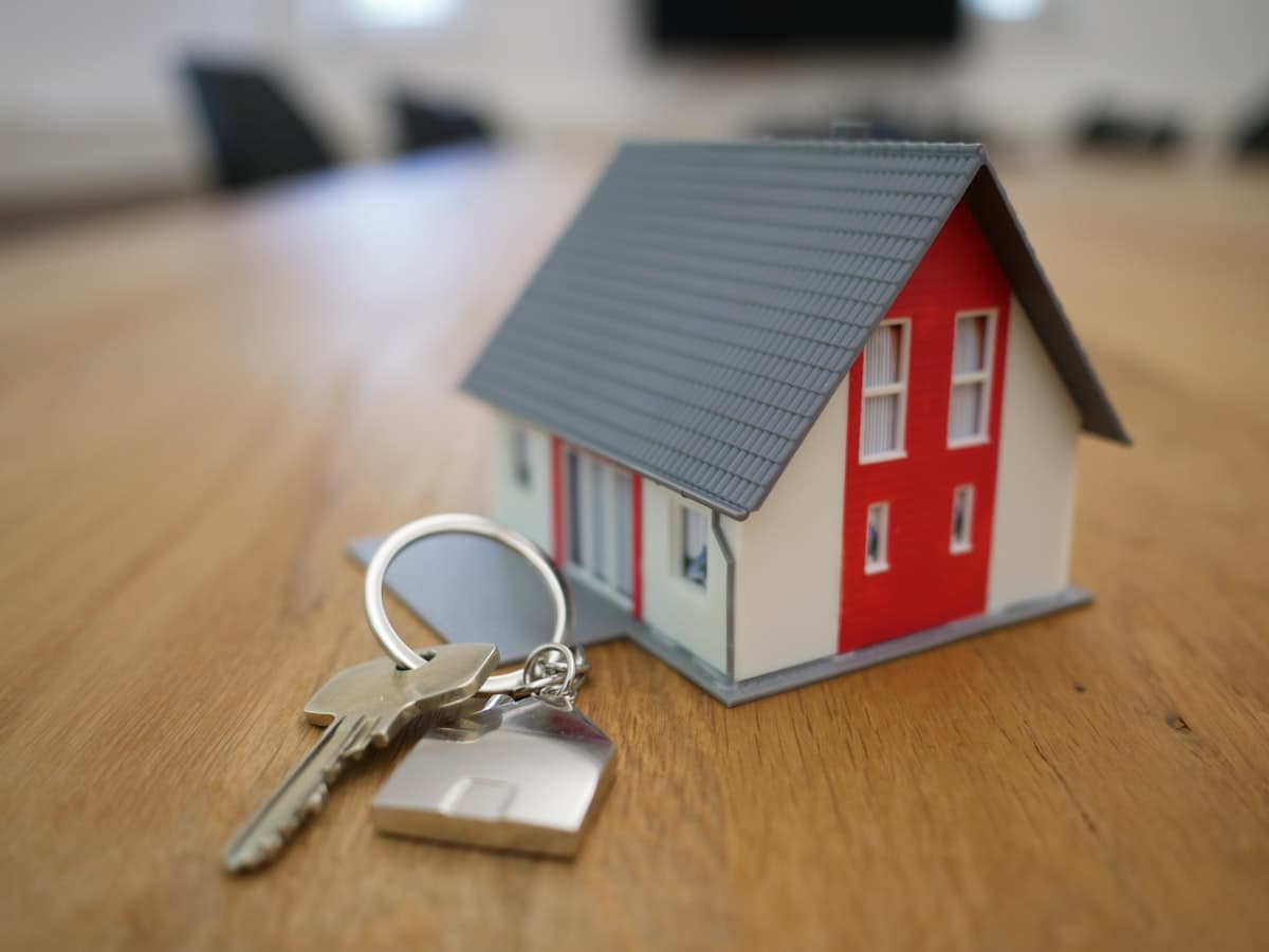 A set of house keys beside a small model house on a wooden table